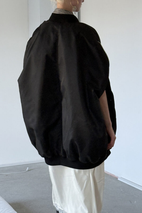 Back view of a model wearing the MARIOS black Uovo bomber jacket, showing its oversized cocoon silhouette, centre back seam and gathered ribbed hem.
